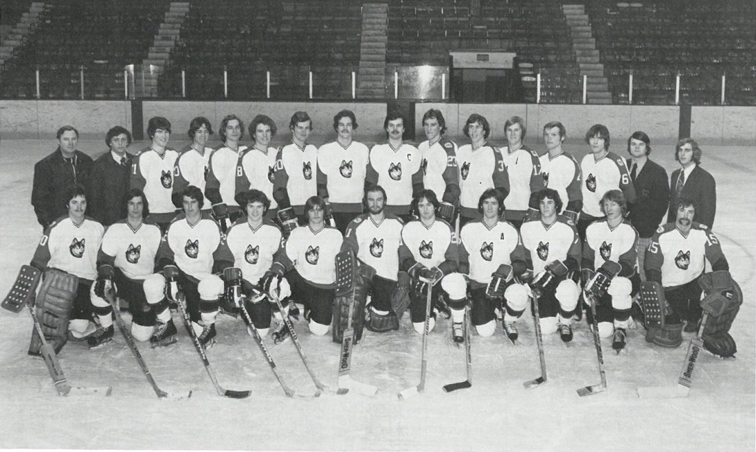 A black and white photo of a men's hockey team and coaches with Huskies on their jerseys