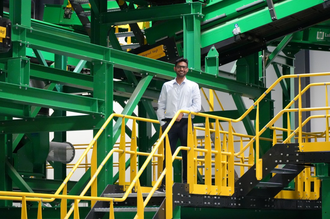 A man stands at the top of a yellow stairwell with his hand on the railing inside an industrial plant.