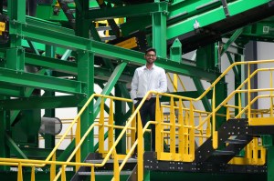 A man stands at the top of a yellow stairwell with his hand on the railing inside an industrial plant.