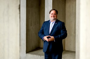 A middle-aged man in a navy suit and blue shirt poses for a photo among cement columns.