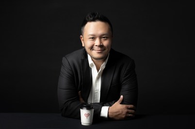 Edward Tirtanata sits at a table in a black suit, with a cup of coffee resting on the table.