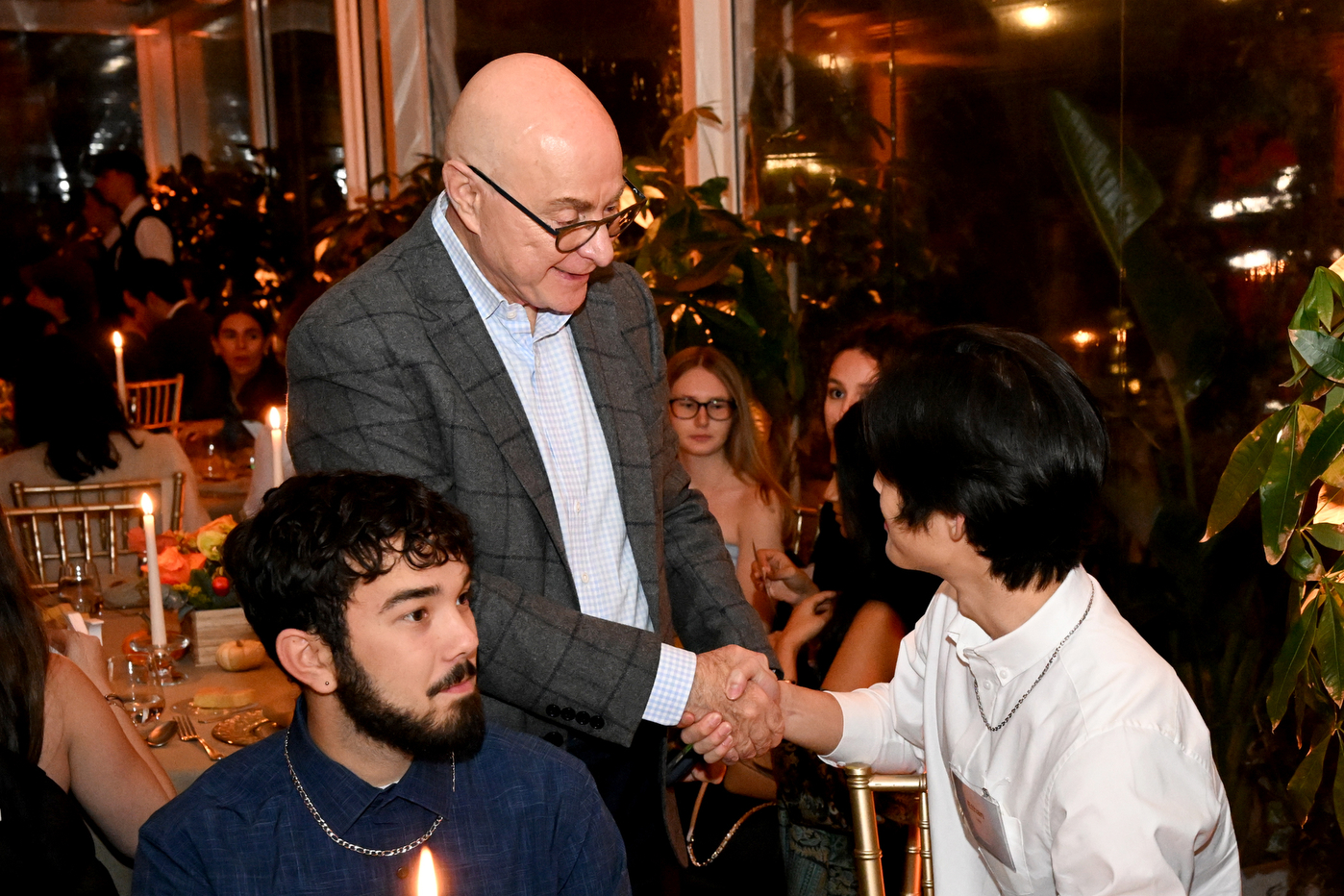 President Aoun shakes a student's hand, while that student is seated at a round table.