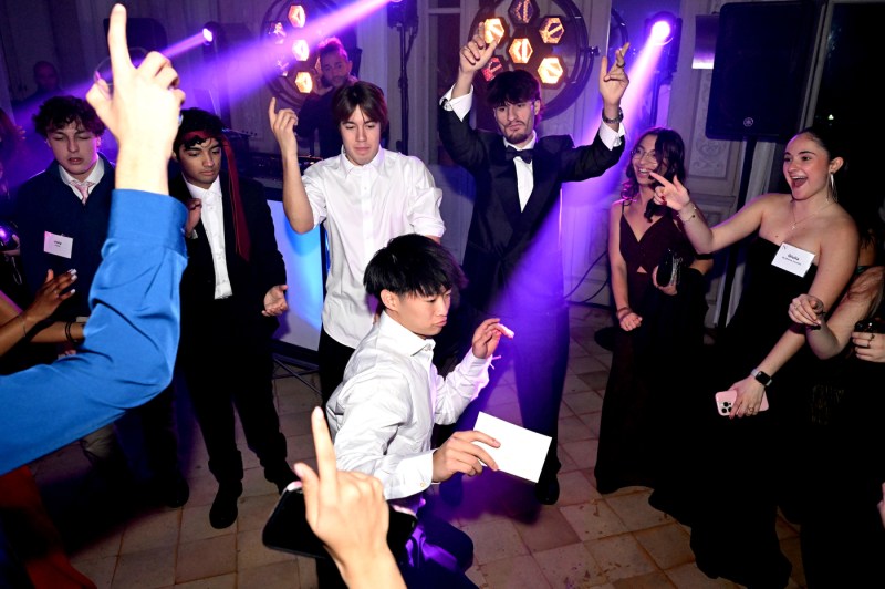 Students dance on a dance floor with purple light shining on them.