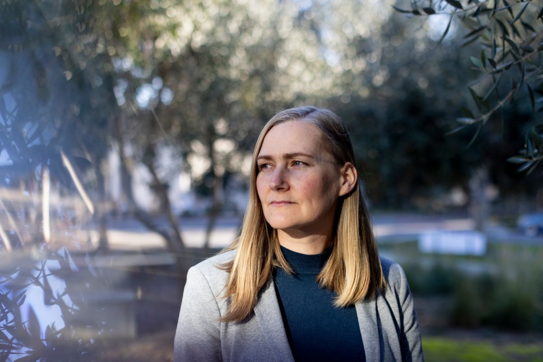 Martha Johnson, associate professor political science, looks over her right shoulder against a woody backdrop.