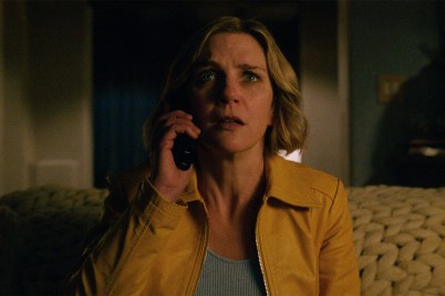 Actress Rhea Seehorn portrays Carol Sturka in "Pluribus," sporting short blonde hair and a yellow jacket with a phone pressed to her ear and a frightened expression on her face.