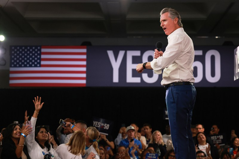 Gov. Gavin Newsom speaks during a campaign event on Proposition 50, which is displayed next to an American flag in the background.
