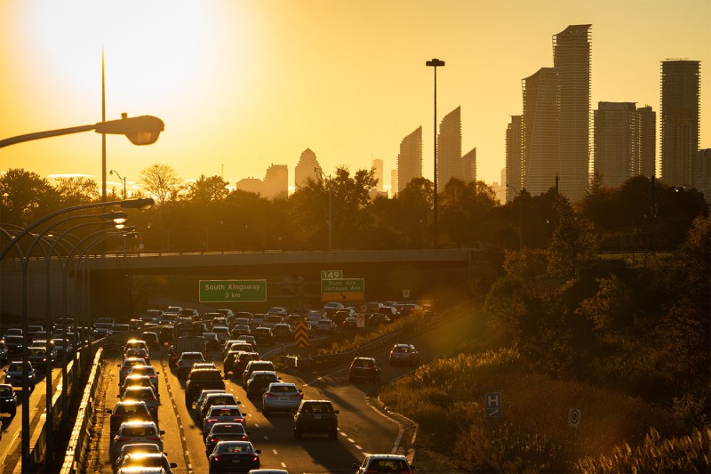 The Toronto skyline during rush hour traffic, with the sun setting in the background.