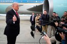 President Donald Trump gesturing to a group of reporters in front of a teal-colored jet engine.