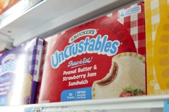 A red box that says 'Uncrustables' on it in blue with a picture of a round, crustless sandwich, filled with peanut butter and jelly.