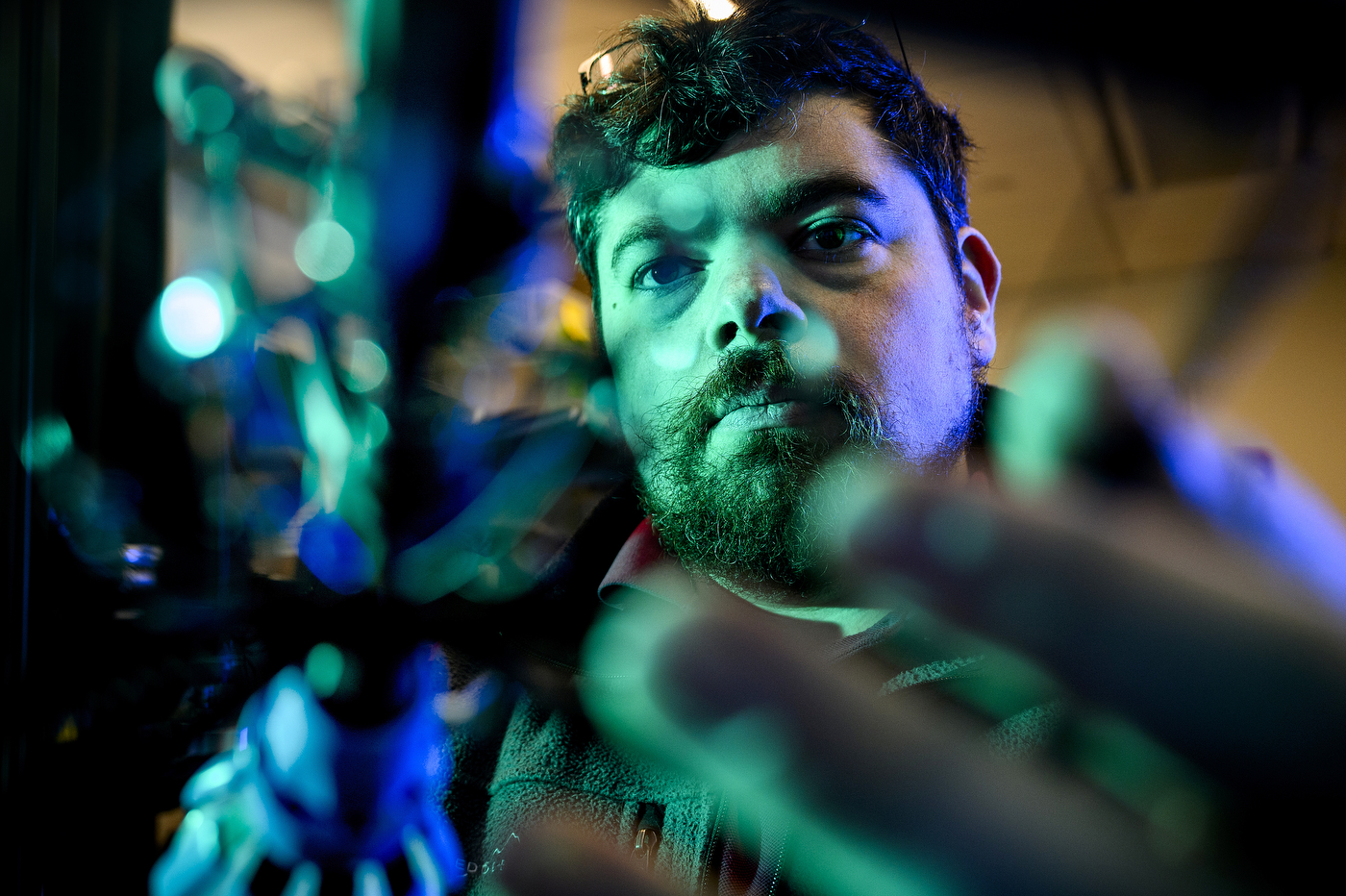 Jeffrey Lipton illuminated by blue and green lighting looking at lab equipment in the foreground.