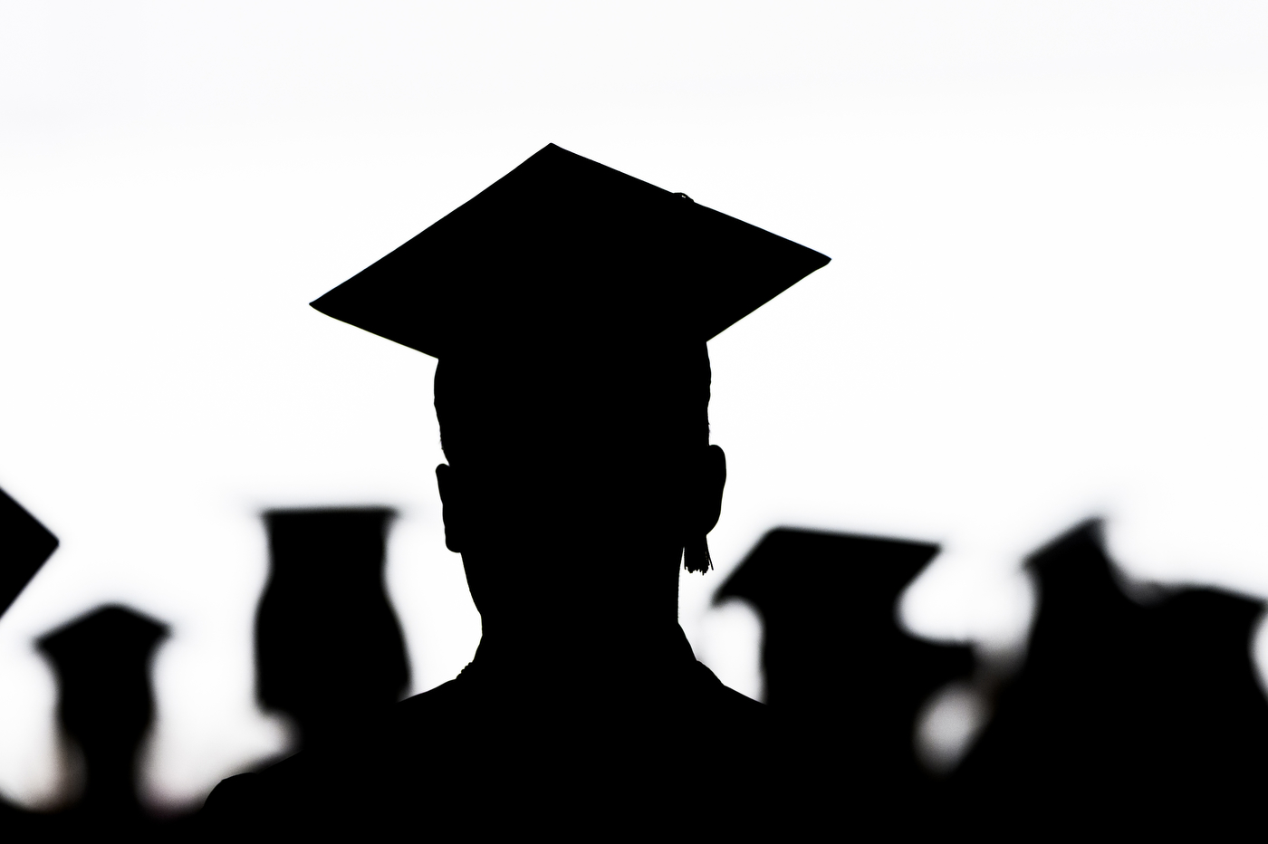 Silhouettes of graduates in caps and gowns against a white background. 