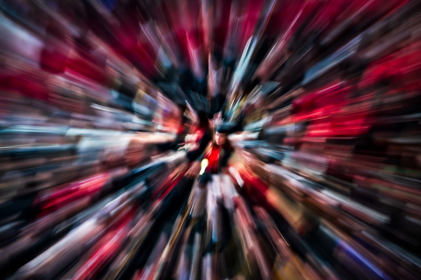 Abstract motion blur of red, blue, and pink radiating outward from a blurry graduate wearing a cap and gown in the center, creating a dynamic zoom effect.