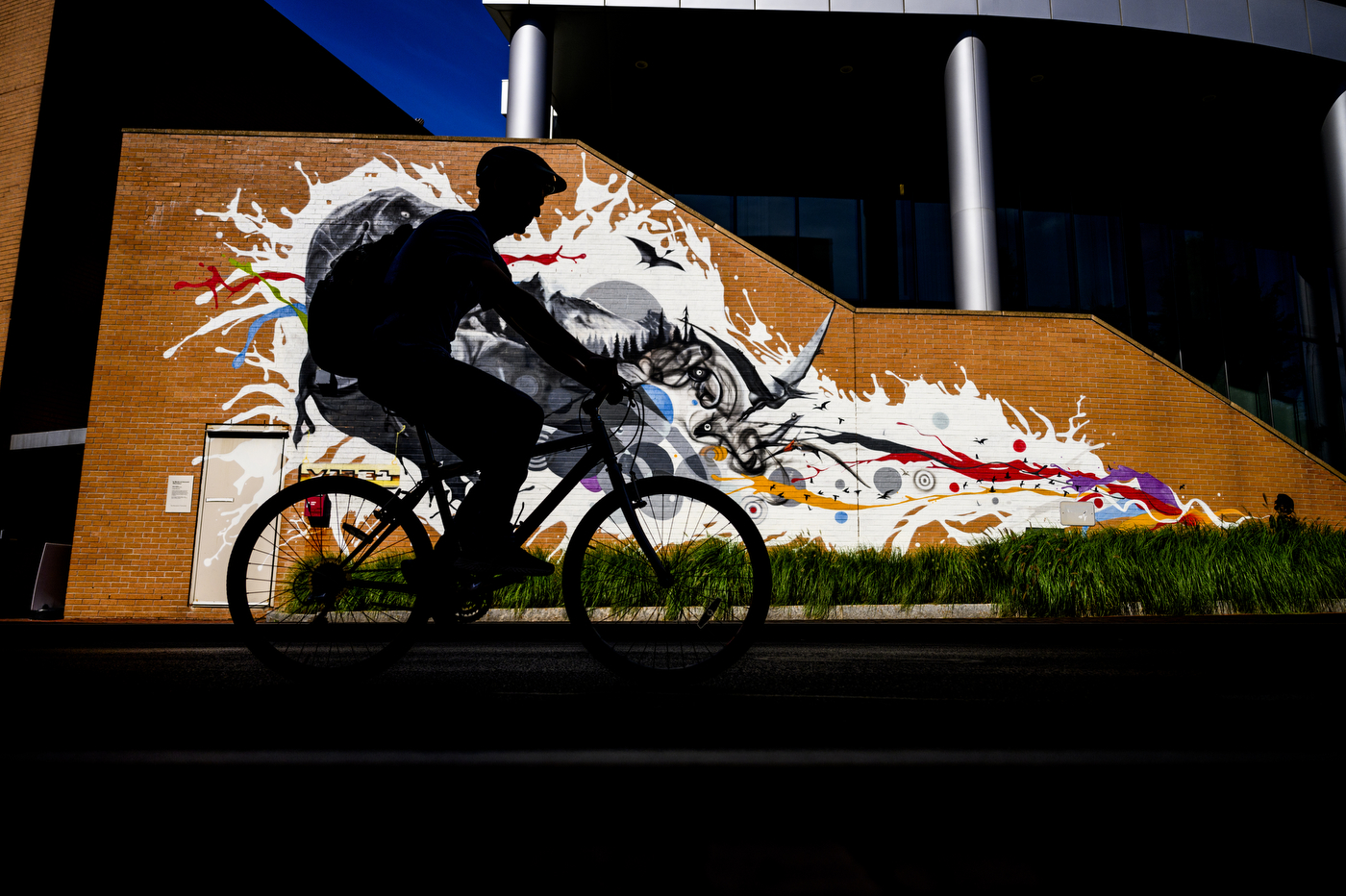 Silhouette of a person riding their bike in front of a mural painted on a brick wall. 
