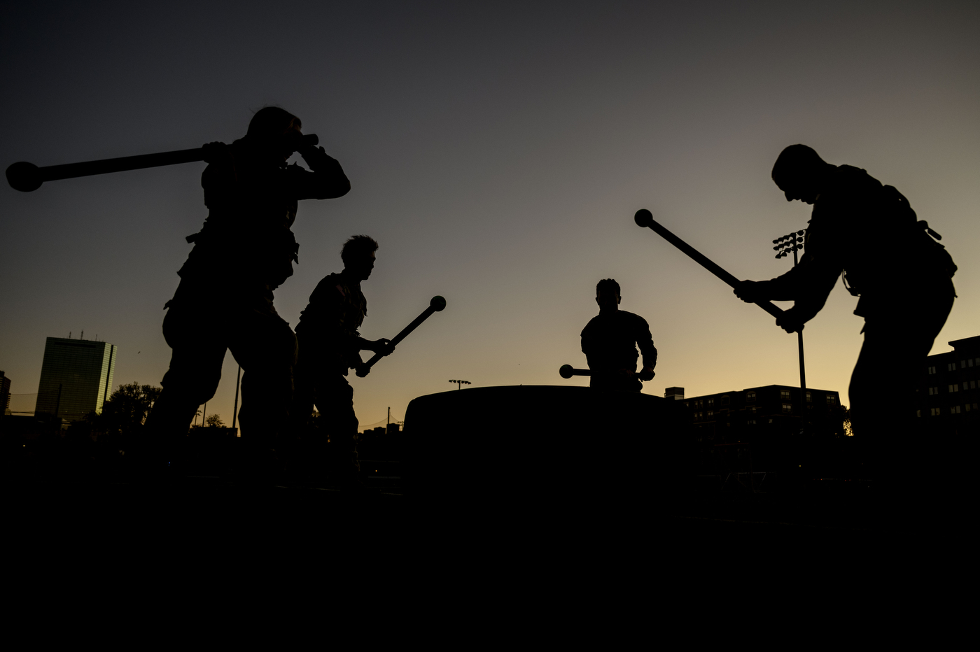 Silhouettes of four ROTC members swinging sticks with balls at the end at sunrise on Carter Field. 