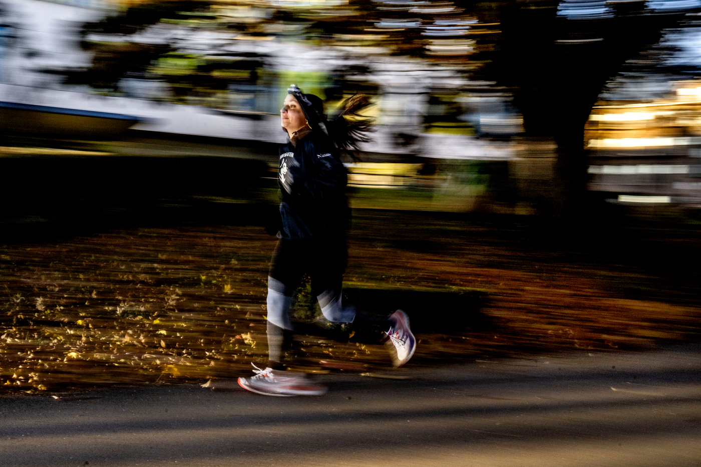 A runner in a Northeastern sweatshirt jogs through autumn leaves with a motion blur suggesting speed and movement.