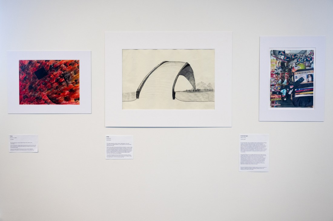 Three student artworks are mounted on a gallery wall, including an abstract red piece, a minimalist black-and-white drawing, and a collage-style image.