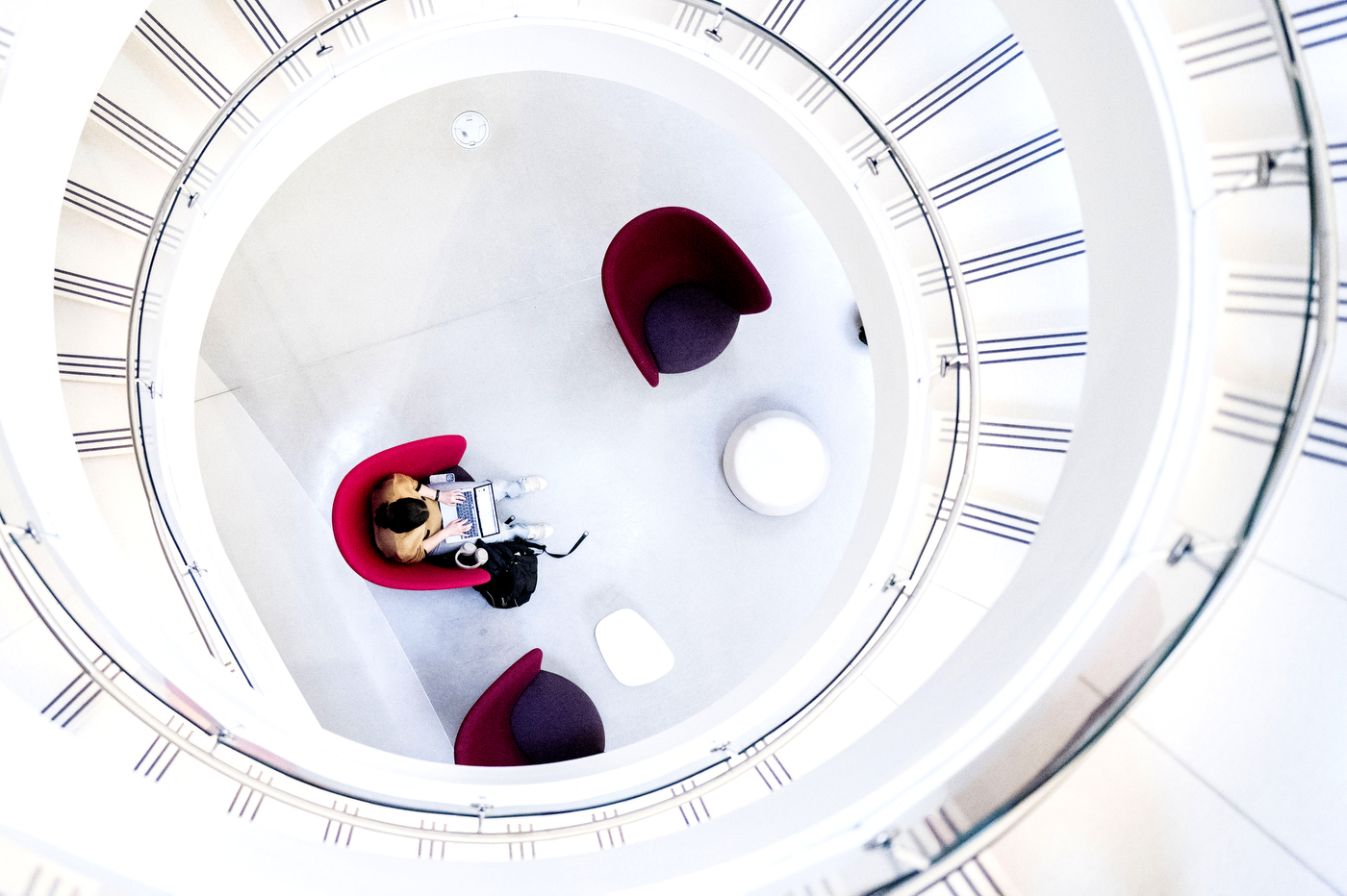 Aerial view of a white spiral staircase and a student studying in a pink chair.