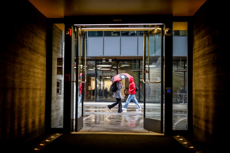 A photo is shot through the doors of EXP as two students walk outside in the rain. 