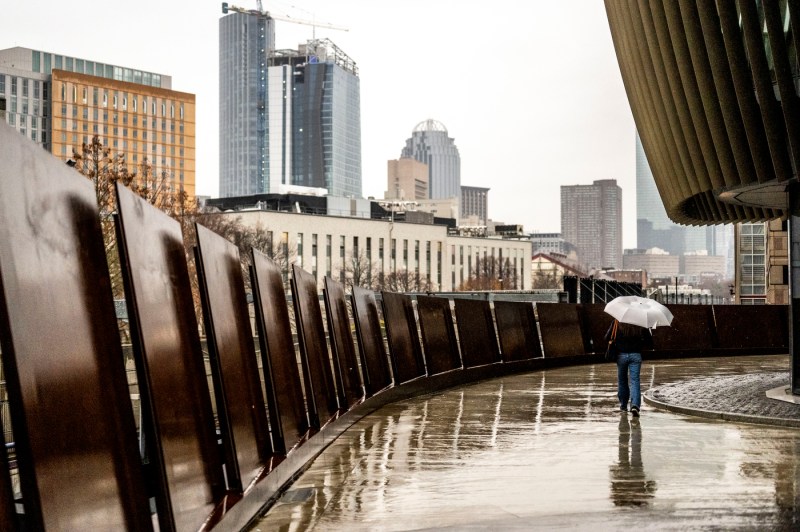 A student with an umbrella walks into ISEC. The Boston skyline is seen in the background. 