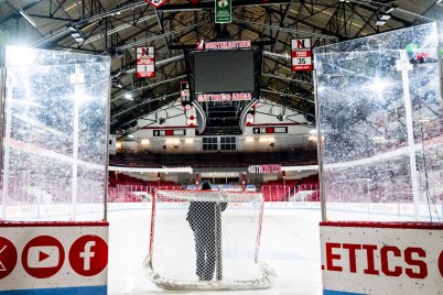 A person stands in front of a hockey net on the ice at Matthews Arena.