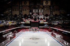 Overhead view of an empty ice hockey arena showing a pristine white rink surrounded by red seating and championship banners hanging from the rafters.