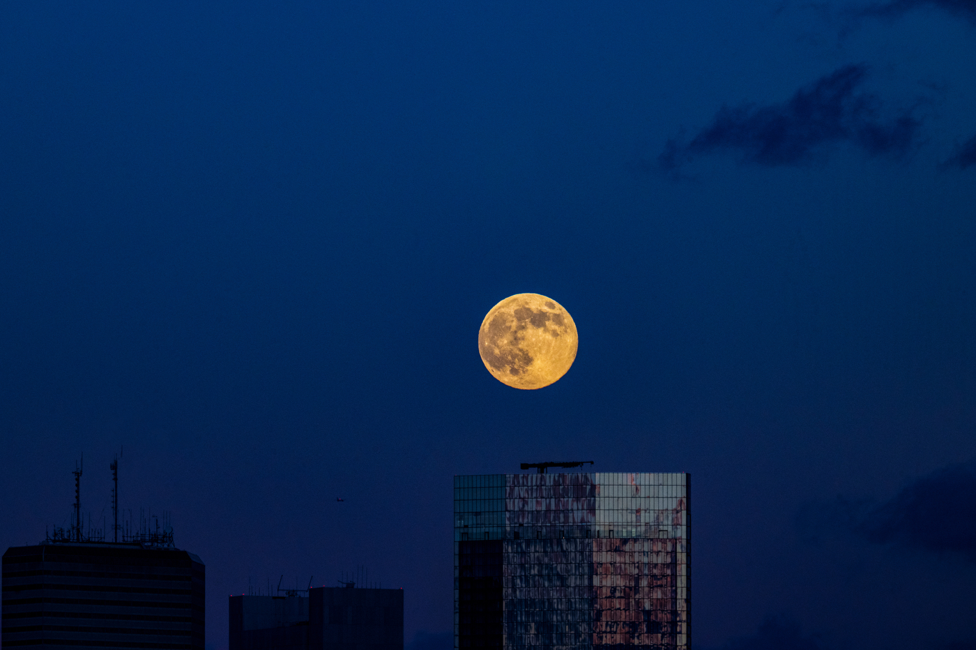 A large full moon rises over a skyscraper against a dark blue sky in Boston.