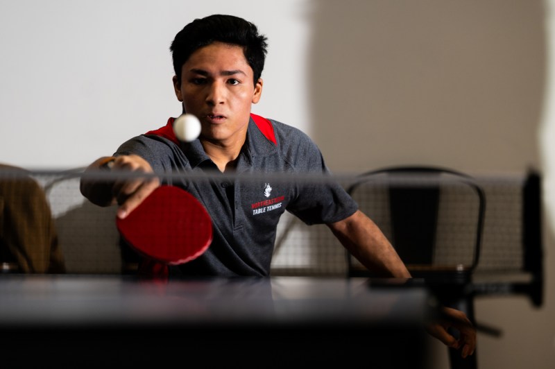 A person reaches out with a paddle to hit a table tennis ball. 
