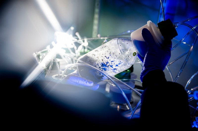 A close-up of a hand holding a piece of lab equipment that is shaped like a bottle. 