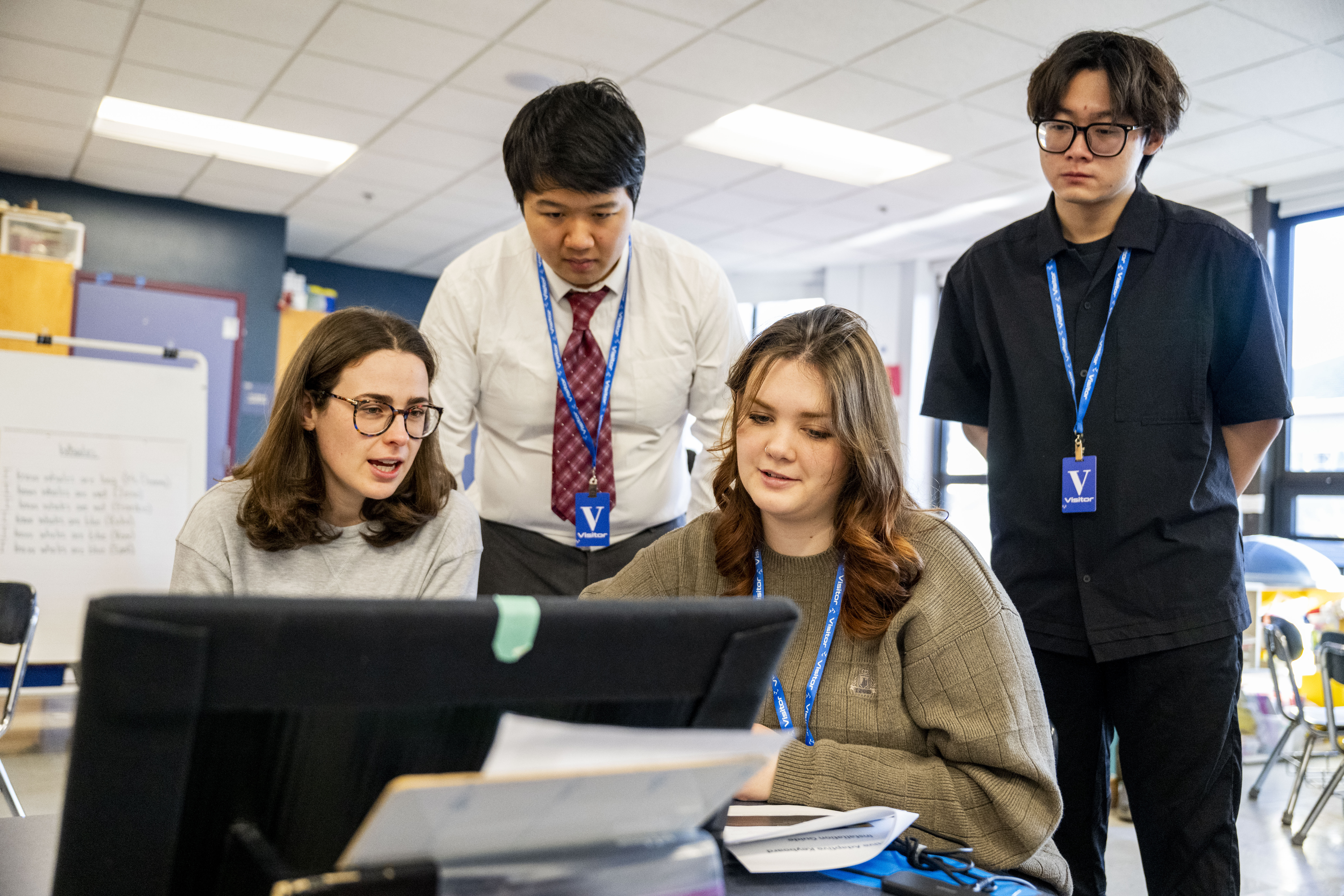 A group of four people gather around an interactive keyboard to work on it, some standing and some sitting.