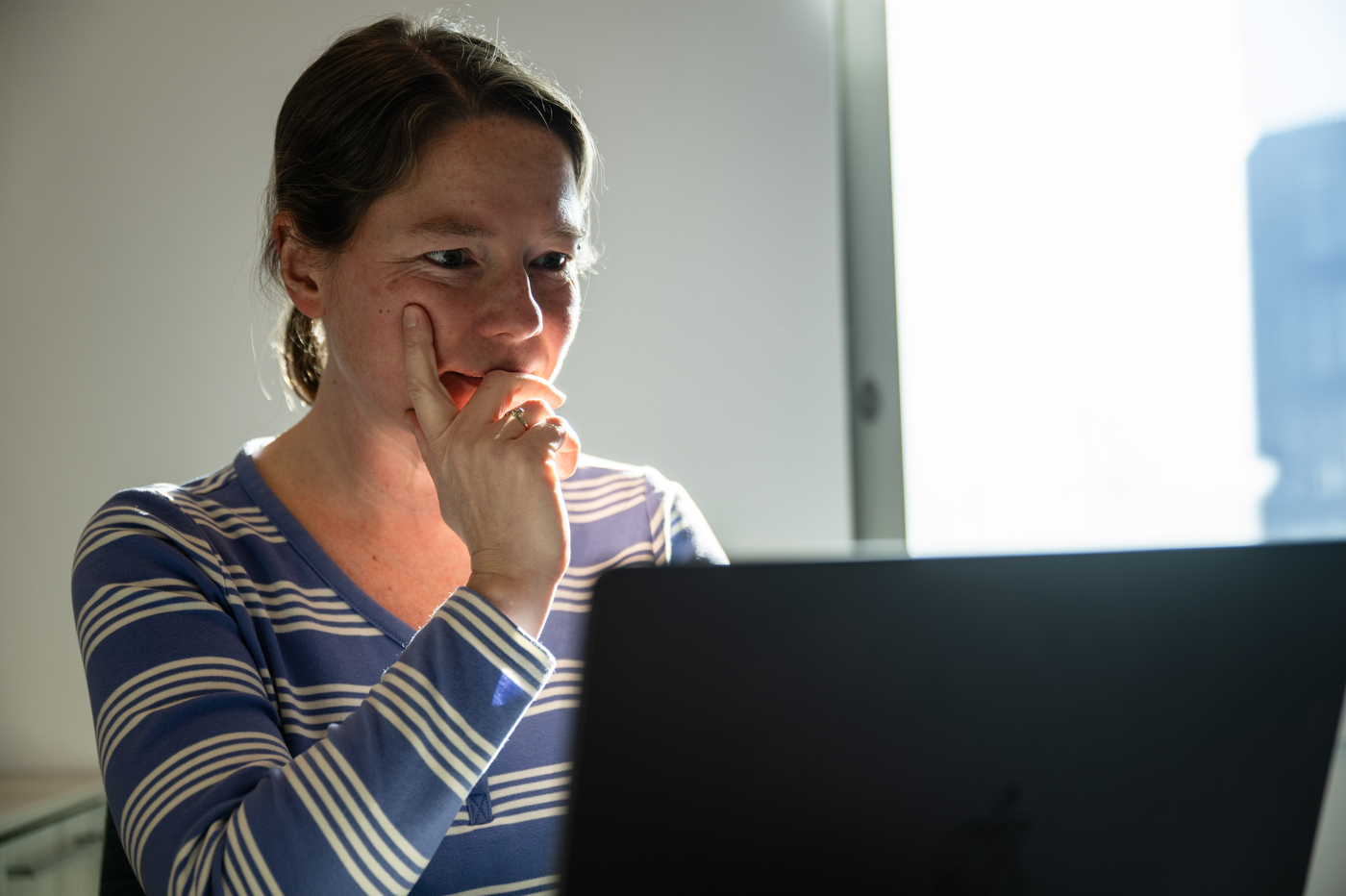 A woman in a striped t-shirt looks at a laptop screen.