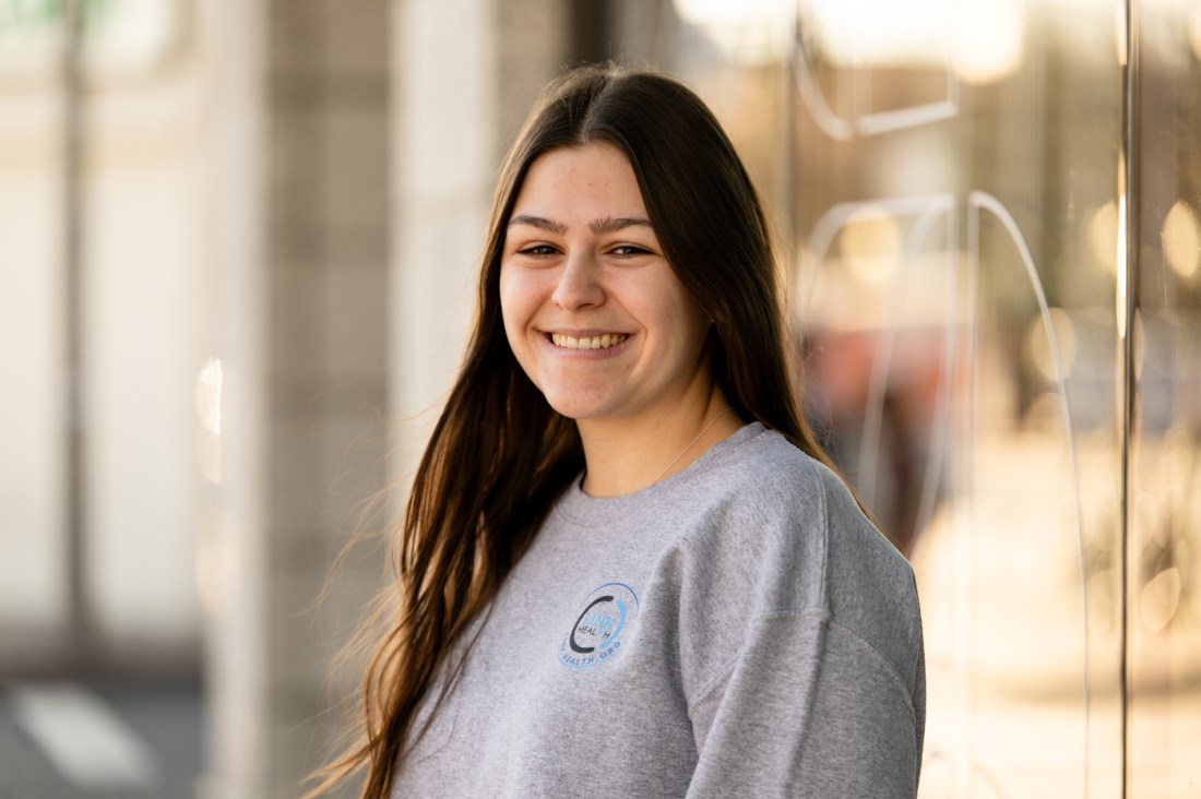 Annamarie Rapa smiling in a grey sweatshirt, standing outside. 