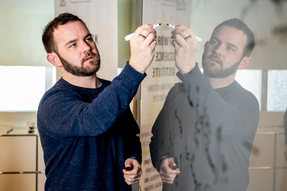 Brennan Klein uses a marker on a dry erase board in a classroom.