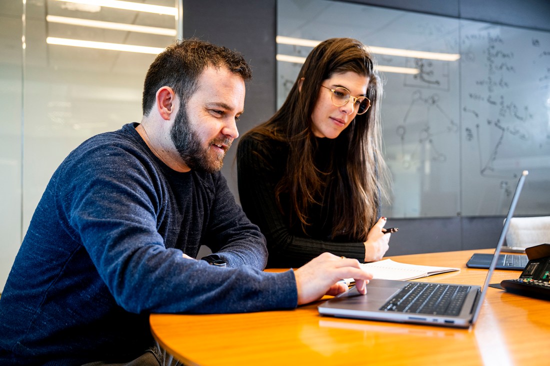 Brennan Klein works at a computer alongside Maddalena Torricelli. Behind them is a dry erase board with figures of networks.
