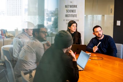 A group of people sit around a wooden table.