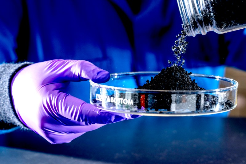 Close up of a globed hand pouring artificial turf into a glass plate.