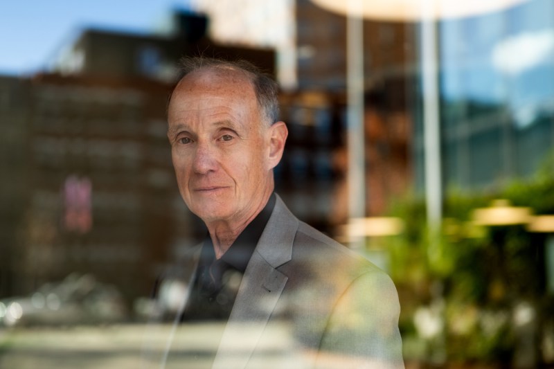 A man who is balding wears a somewhat neutral expression. He is wearing a gray blazer.