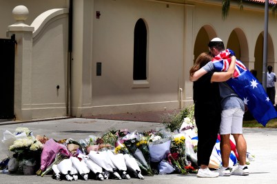Two people embrace in front of flowers that had been laid for victims of a mass shooting.