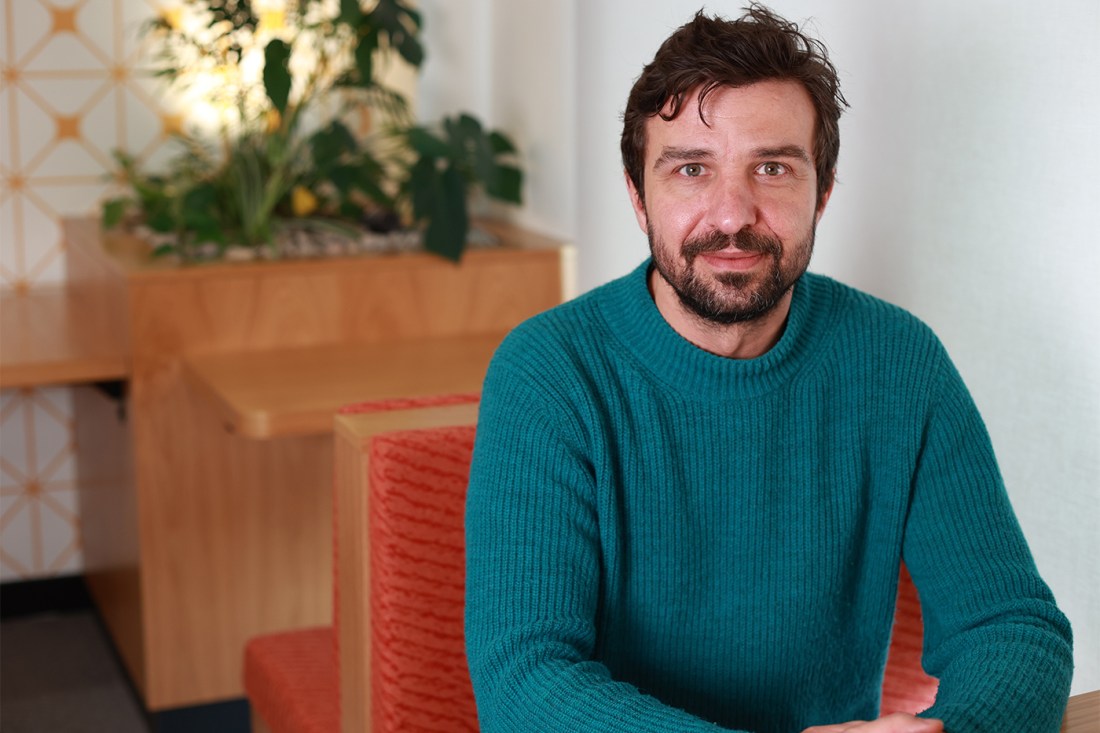 A man in a turquoise jumper sat on an orange cushioned seat