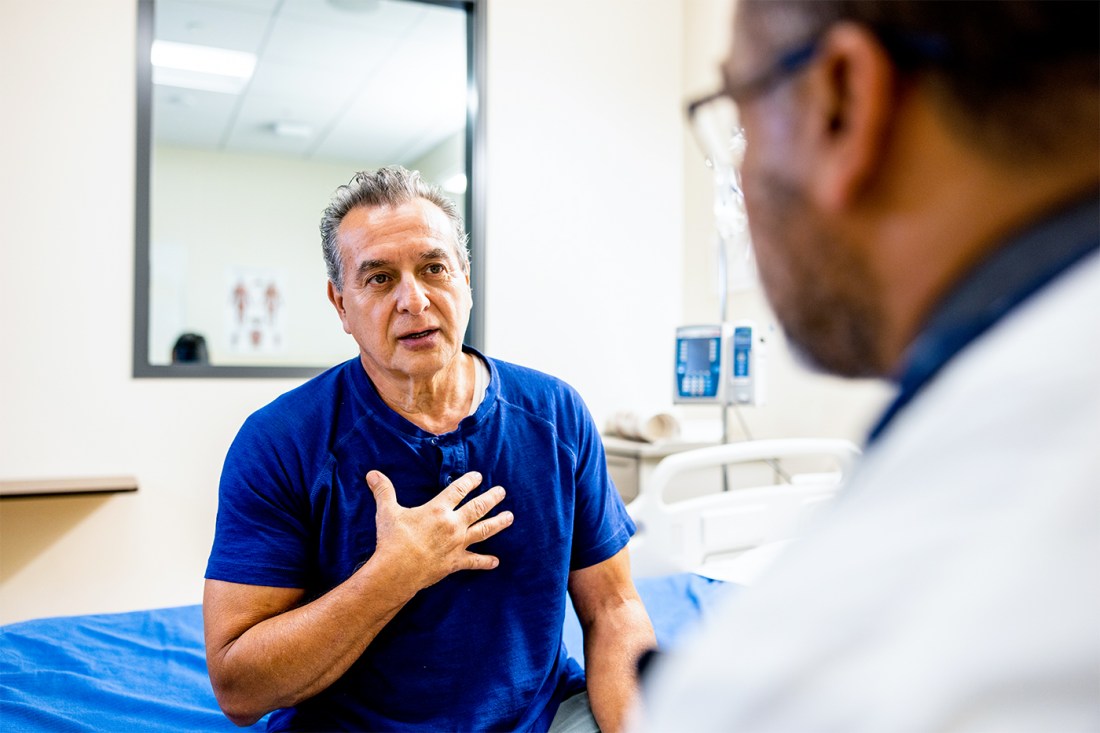 An older man gestures while speaking to a physician, whose face is viewed from the side.