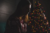 A person sitting in front of a Christmas tree in a dimly lit room looking sad.