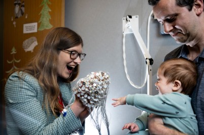 A parent holding a child, who reaches out for a researcher holding an EEG cap
