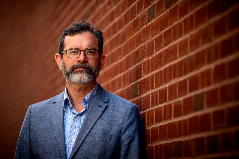 Portrait of Matthew Eckelman standing next to a brick wall. 