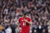 A professional footballer in a red jersey lowers his head on a field. The background is a blur of spectators.