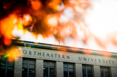 The exterior of an academic building displaying "Northeastern University." Autumnal leaves shine in the foreground.