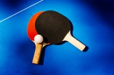 Two ping pong paddles overlapping on a ping pong table with a white ping pong ball.