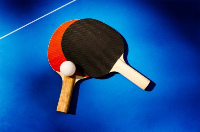 Two ping pong paddles overlapping on a ping pong table with a white ping pong ball.