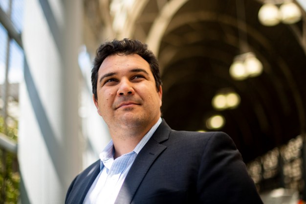 Khusal Safi has dark brown hair and is wearing a black blazer. He is looking off into the distance.