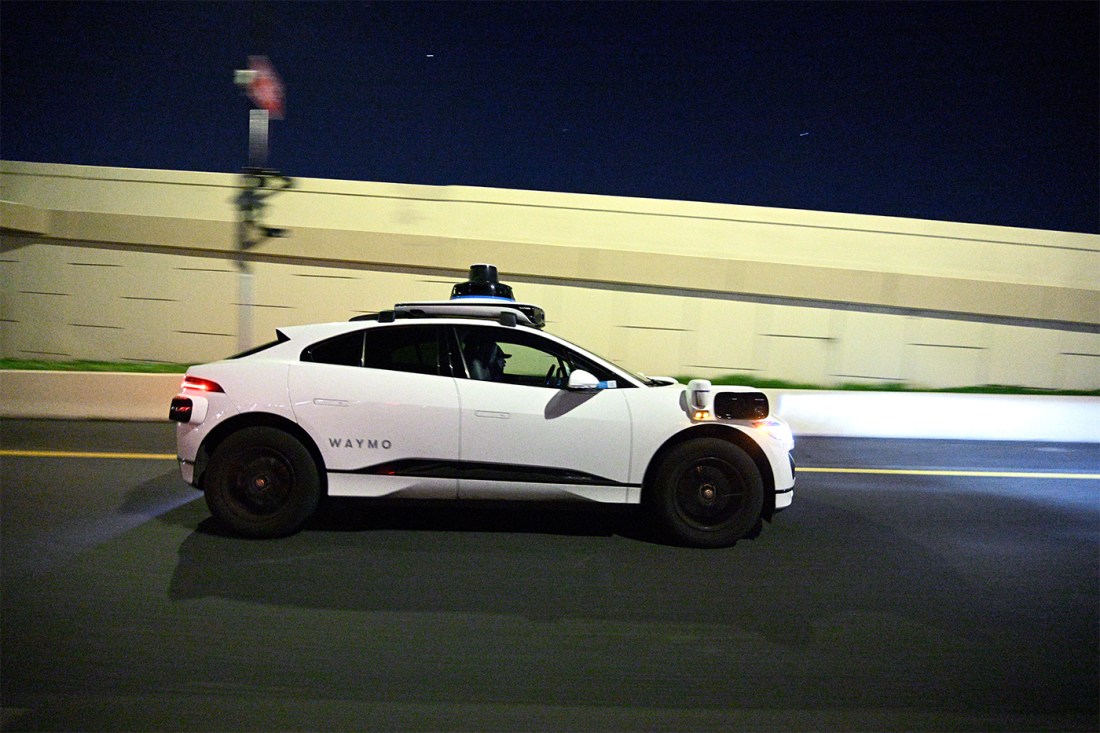 A Waymo autonomous ride-hailing electric Jaguar vehicle makes its way along a roadway.