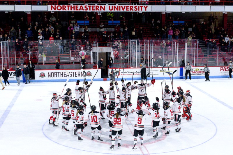 Hockey players hold their sticks up in the air as they celebrate on the ice.