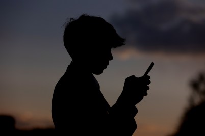 The silhouette of a young person holding a cellphone up in front of their face.